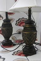 Two side table lamps with dark textured lattice bases and white fabric shades, cords visible, positioned in front of floral wallpaper.