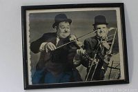 Framed black and white photo of Abbott and Costello, one holding a violin and the other a trombone, both wearing bowler hats.