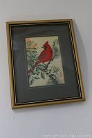 Framed miniature woven picture of a red cardinal on a branch with leaves and flowers, gold-tone frame and dark mat.