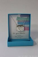 Front view of the silver plated heart-shaped pendant necklace inside the original blue presentation box with a branded insert card.