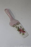 Top side view of the vintage pie server showing floral rose pattern with gold accents and pink handle.