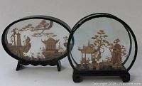 Pair of vintage Chinese carved bamboo figures in wooden cased stands with glass fronts, one oval and one rounded, depicting traditional landscapes and figures.