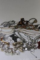 Overhead view of various vintage costume jewelry necklaces spread out, showing a variety of materials including faux pearls, metal chains, shells, and colorful beads.