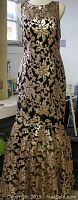 Front view of sleeveless gold sequin mermaid ball gown on a dress form showing floral pattern and mermaid hem with small train.