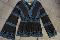 Top down photo of the black blouse with blue lace trim, showing full front with bell sleeves and lace detail.