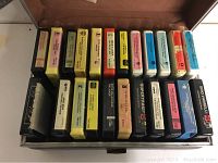 Array of 8 track tapes neatly arranged side by side inside a storage case showcasing various colors and labels.