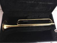 Brass bugle resting inside the black plush-lined case, showing overall condition and dented areas.