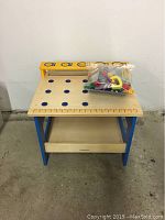 Front view of wooden toy workbench with plastic bag of toy tools on top against white background