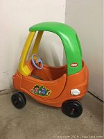 Side view showing green roof, yellow frame, orange body with Dora sticker, blue steering wheel, black wheels