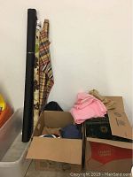 View of fabric rolls and folded fabrics including black, floral, plaid, pink, and tan fabrics