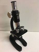 Front view of black and chrome hobby microscope showing magnification markings and stage with clips