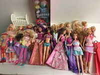 Wide view showing approximately 19 Barbie dolls in assorted outfits and various hair colors along with a doll cradle and boxed Easter doll