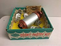 Vintage Mirro Cooky Pastry Kit contents arranged inside original box, showing cylindrical press with red ends and metal shaping discs.