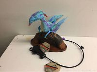 Full view of Disney Banshee toy mounted on a brown perch with attached wired remote control seen on white table.