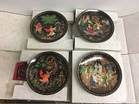 Four Bradford Exchange collectible plates displayed in their original white foam insets and boxes. Plates feature detailed artwork depicting classical or folklore scenes with multiple characters in colorful traditional attire against dark backgrounds, surrounded by ornate borders.