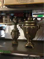 Front view of vintage samovar and teapot warmer on metal shelf.