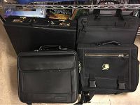Three black briefcases and laptop bags placed side by side showing overall exterior design, handles, and closures.