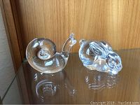 Photo of both Steuben crystal figurines, snail and bunny, on reflective surface showing overall shape and clarity