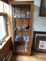 Front view of the glass curio cabinet filled with various glassware and decorative items on the shelves.