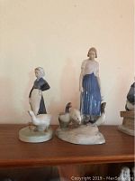 Two porcelain figurines of Danish women with geese standing on a wooden surface, showing full frontal view