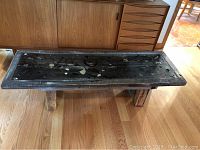 Front and side view of rectangular wooden table with mixed embedded objects in top surface against wood floor and mid-century cabinet in background.