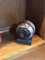 Polished stone sphere with natural multicolor banding on black base.