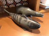 Full side view of both the stone bear and wooden fish sculptures placed on a surface with background tiles.