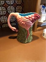 Side view showing pink flamingo body, green leafy base, and blue interior inside pitcher.