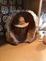 Full view of the carved wooden bust of a man wearing a hat placed on a counter with a tiled backsplash.
