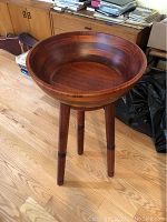 Wooden stool with deep bowl seat, angled view showing wood grain and three legs.