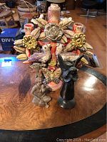 Front view of three southwestern decorative items on a wooden table: multicolored candleholder with birds and flowers, black bird candleholder, and seated figurine.