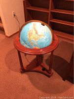 Front view of illuminated globe in wooden stand, power cord visible