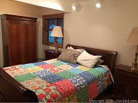 Queen sleigh bed with quilt, pillows, armoire and right-side nightstand with brass lamp visible