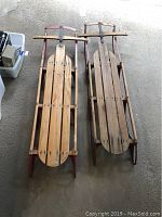 Top view of the pair of vintage wooden sleds with red metal frames on a concrete floor.