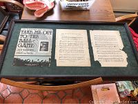 Full view of the framed sheet music laid flat on a table, showing all three pages inside the frame.