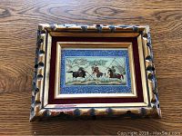 Full view of miniature Persian horsemen polo painting in ornate carved and gilt wooden frame on wood surface.