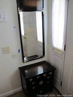 View of the full cabinet and wall mirror installed together near an entry door, showing black lacquer finish and gold decorative hardware.