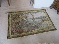 Full view of the tapestry laid on the floor showing its size and detail of the scenic outdoor panoramic view with floral and stone elements.