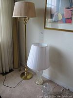 Photo showing 57-inch tall brass floor lamp with pleated shade next to clear glass table lamp with pleated shade and small glass lamp at floor level.