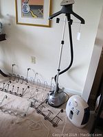 Full view showing Conair clothes steamer with adjustable hanger and steam nozzle, surrounded by multiple over-the-door hangers in black, chrome, and white.
