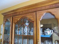 Peacock fine china tea set displayed inside wooden china cabinet with glass doors showing multiple pieces including teapot and cups with detailed colorful peacock and floral designs.
