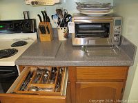 The kitchen countertop showing the Frigidaire convection oven, stacked plates on top, a knife block with knives, and a crock with kitchen utensils.