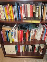 Full bookshelf with multiple rows of assorted books including cookbooks, reference, and fiction. Books on top row excluded by seller.