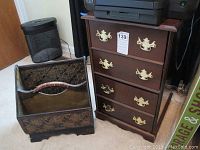 Wood file cabinet and woven magazine rack on floor near a door and waste basket.