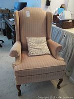 Full view of beige wingback chair with wooden legs and rolled arms in indoor setting