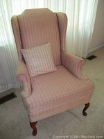 Front left-side view of the pink wingback chair with matching pillow, showing rolled arm and wooden leg.