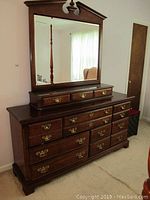 Front view of large wooden dresser with attached mirror and jewelry box topper on top, showing brass handles and polished wood finish with surface wear.