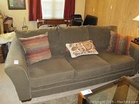 View of entire sofa showing upholstery, cushions, and pillows in a wood-paneled room. Cushion repair noted on one seat cushion.