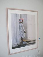 Framed print with image of a girl in a white dress and hat standing by columns holding a yellow umbrella.