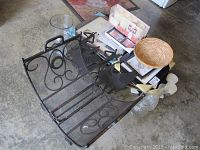 Photo showing metal log holder with scrollwork, several picture frames stacked, clear glass vases, and candles on floor surface